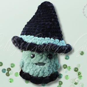 May include: A handmade crochet mushroom figure in shades of teal and navy blue. The mushroom has a whimsical design, featuring a pointed hat and a smiling face. The background is a light green with scattered sequins.