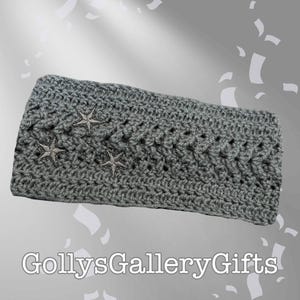 May include: A gray crocheted headband with three embroidered silver stars. The headband is made of a textured yarn and features a decorative stitch pattern. The text "GollysGalleryGifts" is at the bottom.