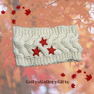 May include: Cream-colored knitted headband with a cable knit design. Three red embroidered stars are centered on the front. The headband is a cozy accessory for cooler weather. The text "GollysGalleryGifts" is at the bottom.