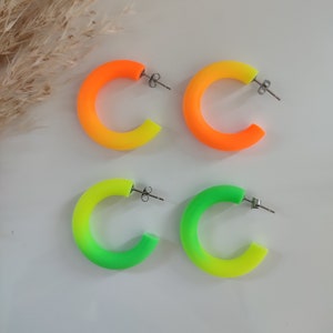 May include: A pair of neon yellow and orange hoop earrings and a pair of neon green and yellow hoop earrings. The earrings are made of a smooth, plastic-like material.