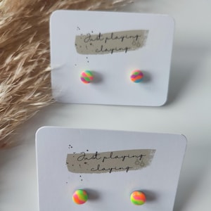 Op de afbeelding: Een paar regenboog-wervel oorbellen op een witte kaart met de tekst "Just playing with claying".