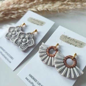 Peut inclure: Deux paires de boucles d'oreilles en argile faites à la main. La première paire présente un motif floral blanc. La deuxième paire présente un motif en éventail blanc avec un cercle en bois brun au centre. Les deux paires ont des crochets d'oreille dorés. Accessoires en argile faits à la main www.JustPlayingClaying.etsy.com