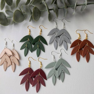 May include: Five pairs of dangle earrings with a leaf design. The earrings are made of polymer clay and come in five different colours: green, grey, brown, burgundy, and beige.