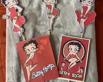 May include: Four red and black Betty Boop character cutouts on sticks. The cutouts feature Betty Boop in different poses, including one with hearts and the text "Betty Boop".