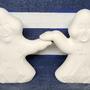 May include: Two white ceramic ghost figurines with outstretched arms and open mouths. The ghosts are standing on a blue and white striped background.