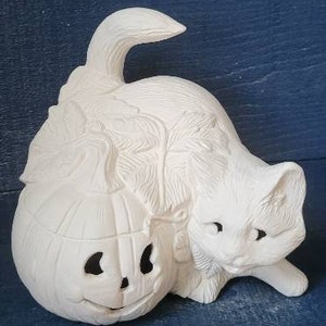 May include: White ceramic bisque figurine of a cat peeking out from behind a pumpkin. The pumpkin has a carved jack-o'-lantern face.