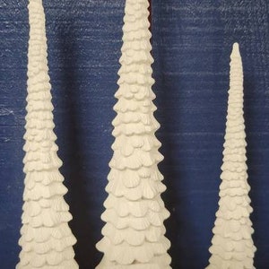 May include: Three white ceramic Christmas trees of varying sizes. The trees are made of layered, scalloped shapes that resemble pine branches.