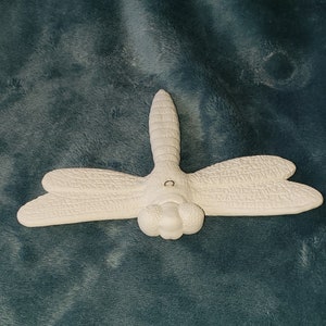 May include: White ceramic dragonfly wall hanging with a small metal ring for hanging. The dragonfly has detailed wings and a textured body.