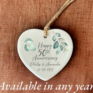 May include: White ceramic heart ornament with a green leafy design. It says "Happy 50th Anniversary Philip & Amanda 31-09-1973".