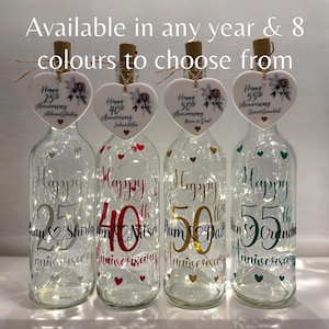 May include: Four glass bottles with cork tops and fairy lights inside. Each bottle has a heart-shaped tag with a floral design and text that says "Happy 25th Anniversary", "Happy 40th Anniversary", "Happy 50th Anniversary", and "Happy 55th Anniversary".