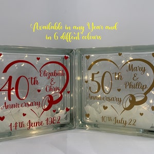 May include: Two glass blocks with lights inside. The left block has a red heart with the text "40th Anniversary Elizabeth & Chris" and the date "14th June 1982". The right block has a gold heart with the text "50th Anniversary Mary & Phillip" and the date "10th July 22".