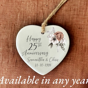 May include: White ceramic heart ornament with a floral design and the text "Happy 25th Anniversary Samantha & Chris 31-10-1998".