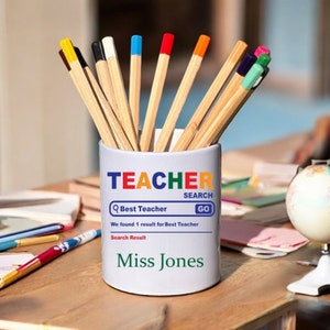 May include: White ceramic pencil holder with the text "TEACHER" in rainbow colours. The holder has a search bar with the text "Best Teacher" and a "GO" button. The search results show "We found 1 result for Best Teacher" and "Search Result". The name "Miss Jones" is displayed below the search results.