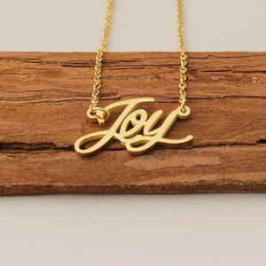 Könnte beinhalten: Goldkette mit einem Anhänger in Schreibschrift 'Joy'.