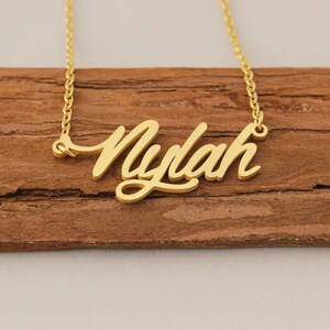 May include: Gold necklace featuring the name "Nylah" in a cursive script.