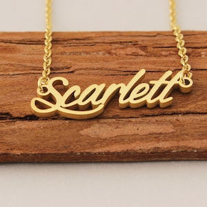 Könnte beinhalten: Goldkette mit dem Namen "Scarlett" in kursivschrift.