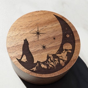 Peut inclure: Une boîte en bois avec un motif de croissant de lune, un loup hurlant à la lune et des étoiles. La boîte est en bois de noyer.