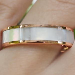 May include: A rose gold band with a white mother-of-pearl inlay. The ring is a simple design with a polished finish.