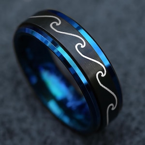 May include: A black ring with a blue interior and a wave pattern. The ring has a silver wave design on the black band. The ring's interior has a blue, iridescent finish.