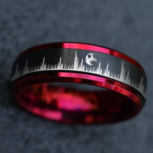 May include: A red and black ring with a silver design. The ring features a black band with a silver skyline and a Death Star graphic. The inner band is a bright red color.