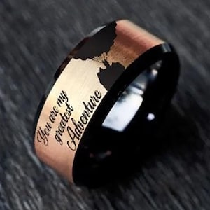 May include: A black and rose gold tungsten carbide ring with the inscription "You are my greatest Adventure".