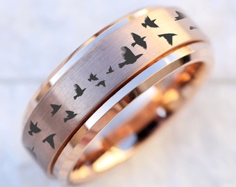 May include: A rose gold tungsten carbide ring with a beveled edge and a band of flying birds engraved on the surface.