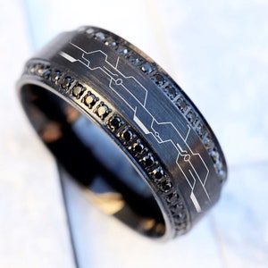 May include: A black ring with a black diamond band and a white circuit board design.