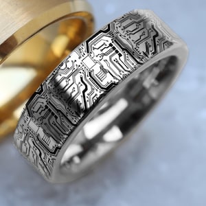 May include: A silver wedding band with a black circuit board design. The band is smooth and shiny.