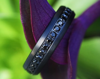 May include: A black ring with a band of small black diamonds set into the metal.