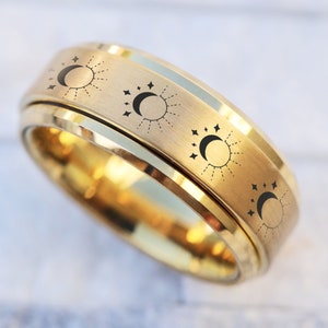 May include: A gold spinning ring with a design of suns and moons with stars around them.