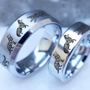 May include: Two silver-colored rings with a polished finish. Each ring features a repeating pattern of black wolf silhouettes around the band. The rings are likely for couples or matching sets, showcasing a nature-inspired design.