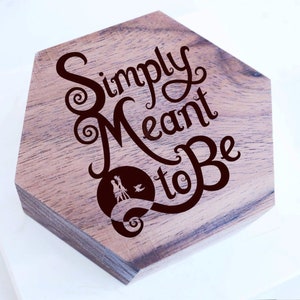 Puede incluir: Una caja hexagonal de madera con un tinte marrón oscuro. La caja presenta una silueta de una pareja caminando por un sendero con las palabras "Simply Meant to Be" en una fuente decorativa.