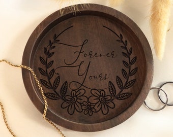 May include: A dark brown wooden ring dish with a floral design and the words "Forever Yours" engraved on the top.