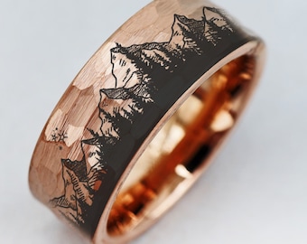 May include: A rose gold wedding band with a hammered finish and a black inlay featuring a mountain range design.