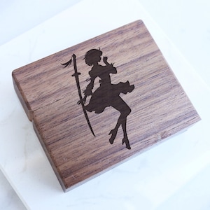 Könnte beinhalten: Eine Holzkiste mit einer lasergravierten Silhouette einer Frau, die ein Schwert hält. Die Frau trägt ein Kleid und hat ihre Haare nach hinten gebunden.