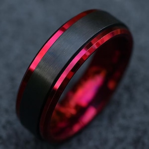 May include: A black ring with a red interior and a red stripe. The ring has a brushed metal finish and a sleek, modern design. The red color provides a striking contrast to the black.