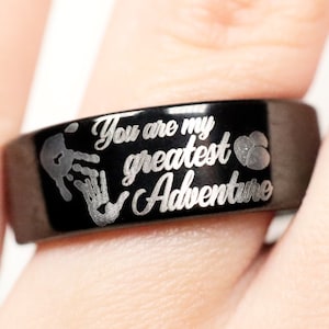May include: Black ring with the inscription "You are my greatest Adventure" and two handprints engraved on the band.