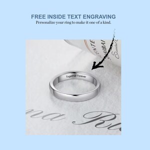 May include: A silver wedding band with the inscription "Together Forever" engraved on the inside. The ring is lying on a white surface.