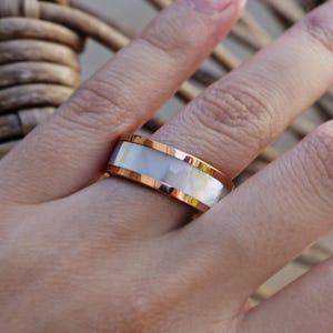 May include: A white and rose gold ring with a white mother of pearl inlay.