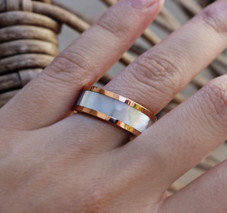 May include: A white and rose gold ring with a white mother of pearl inlay.