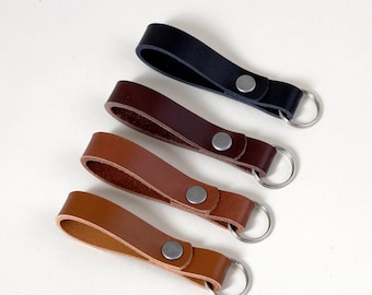 May include: Four leather keyrings with silver key rings. The keychains are in different shades of brown and black.