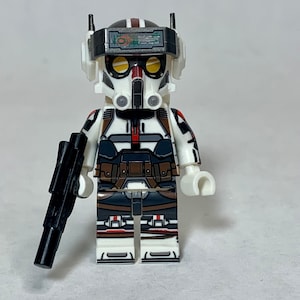 May include: A white and black action figure with a helmet, goggles, and a black weapon. The figure has brown and red accents on the chest and legs. The figure is a toy.