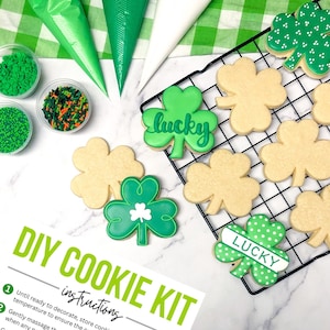 May include: DIY cookie kit with green and white shamrock cookies, green and orange sprinkles, and piping bags. The cookies are decorated with the word "lucky" and white polka dots. The kit includes instructions for decorating the cookies.