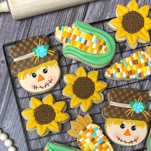 May include: A collection of fall-themed sugar cookies decorated with icing. The cookies include scarecrows, sunflowers, and corn on the cob.