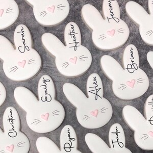 May include: White bunny-shaped cookies with pink heart noses and black whiskers. Each cookie has a name written in black script, including "Sarah", "Heather", "Jeremy", "Brian", "Emily", "Alex", "Christina", "Ryan", and "Jada".
