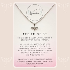 Könnte beinhalten: Eine silberne Halskette mit einem Libellen-Anhänger. Die Halskette liegt auf einer weißen Karte mit dem Text "FREIER GEIST" und einer Botschaft über die Fähigkeit der Libelle, schnell die Richtung zu ändern. Die Karte trägt oben auch den Schriftzug "Wunderia".