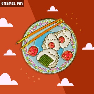 Può includere: Spilla smaltata con un piatto di tre onigiri di cartoni animati, o palline di riso giapponesi, con bacchette. Gli onigiri hanno facce sorridenti e sono decorati con accenti rosa e verdi. Il piatto è blu con un motivo floreale e un bordo dorato.