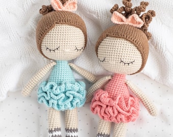 May include: Two crocheted dolls with brown hair and closed eyes, wearing pink and blue dresses with ruffled skirts. The dolls are lying on a white blanket.