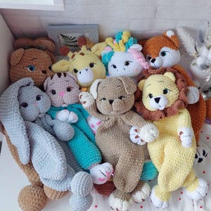 Può includere: Una collezione di animali di peluche all'uncinetto, tra cui una giraffa, un unicorno, un leone, un coniglio, un gatto e un cane. Gli animali sono tutti di colori diversi e hanno espressioni facciali diverse.
