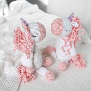 May include: Two crocheted unicorn toys with pink and white yarn. The unicorns have closed eyes and pink yarn for their manes and tails.